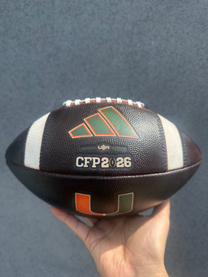 Hand holding a prepped football with 'CFP 2026' branding against a dark background